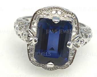 May include: A silver ring with an emerald-cut blue sapphire gemstone set in a filigree design.