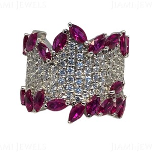 Puede incluir: Un anillo de plata con una banda ancha engastada con pequeñas piedras de circonita cúbica transparentes y un diseño de piedras de forma de marquesa rosas.