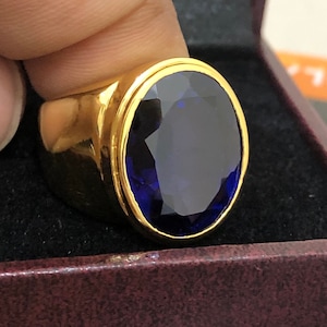 Pode incluir: Um anel de ouro com uma grande gema oval, de cor azul escura.
