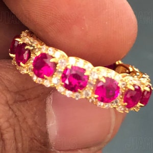 Könnte beinhalten: Ein Goldring mit einer Reihe von rosafarbenen Edelsteinen, die in einer Pavé-Fassung gefasst sind. Der Ring ist von kleineren weißen Edelsteinen umgeben.