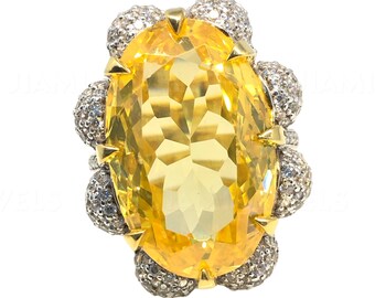 May include: A yellow gemstone ring with a large oval-shaped center stone surrounded by smaller diamonds. The ring is set in gold and has a delicate design.