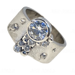 May include: A silver ring with a large, clear, round gemstone surrounded by smaller, clear gemstones. The band of the ring is textured and has a unique design.