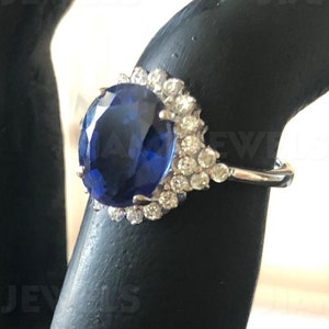 Puede incluir: Un anillo de plata con un gran zafiro azul ovalado rodeado de pequeños diamantes blancos.