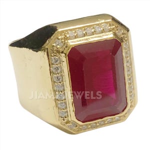 May include: A gold ring featuring a large, rectangular, red gemstone set within a border of small, clear gemstones.