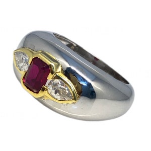 May include: A silver ring with a red gemstone and two smaller clear gemstones. The ring has a gold band.