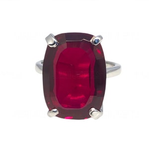 May include: A silver ring featuring a large, oval-shaped, red gemstone.
