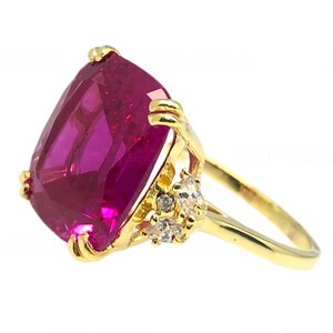 Puede incluir: Un anillo de oro con una gran piedra preciosa rosa de talla cojín, rodeada de piedras preciosas más pequeñas y transparentes.