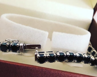 May include: A black onyx tennis bracelet with a silver clasp. The bracelet is made of round black onyx stones set in silver.