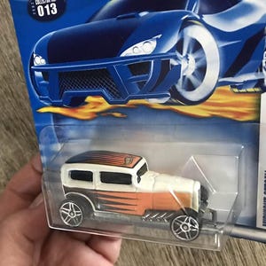 May include: A die-cast Midnight Otto toy car in a clear plastic package. The car is white and orange with black accents and silver wheels. The packaging features a blue car graphic and the text "FIRST EDITIONS" and "MIDNIGHT OTTO".