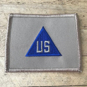 May include: A gray fabric patch with a blue triangle and the letters "US" in white inside the triangle.