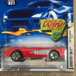 May include: A red and silver Hot Wheels Corvette SR-2 die-cast toy car. The packaging includes the text "RACE & WIN ONLINE" and "2002 FIRST EDITIONS". The car is collector's item number 021.