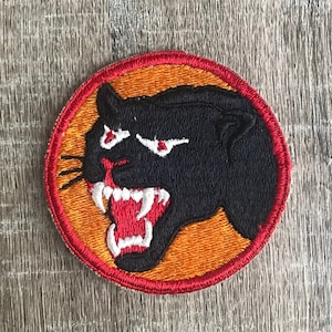 May include: A red, white, and orange embroidered patch with a black panther head snarling with white teeth. The panther has red eyes and is set against an orange background.