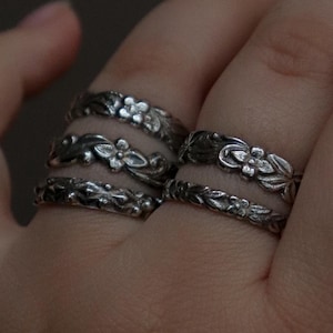 Peut inclure: Une main portant trois bagues en argent avec des motifs floraux. Les bagues sont empilées sur le majeur.