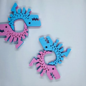May include: Two interlocking dinosaur-shaped toys, one pink and one blue, are made of plastic and are connected by a series of interlocking joints.