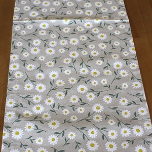 May include: A gray table runner with a white daisy pattern. The daisies have yellow centers and green stems.