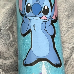 Op de afbeelding: Een blauwe en witte tumbler met een cartoon afbeelding van Stitch uit Lilo & Stitch. De tumbler heeft een glitter afwerking en een bloemenontwerp.