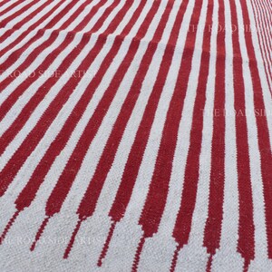 May include: A red and white striped rug with a textured surface. The rug features bold, vertical stripes of red against a white background. The design includes a section with smaller stripes and diamond shapes.