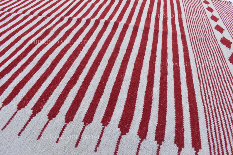 May include: A red and white striped rug with a textured surface. The rug features bold, vertical stripes of red against a white background. The design includes a section with smaller stripes and diamond shapes.