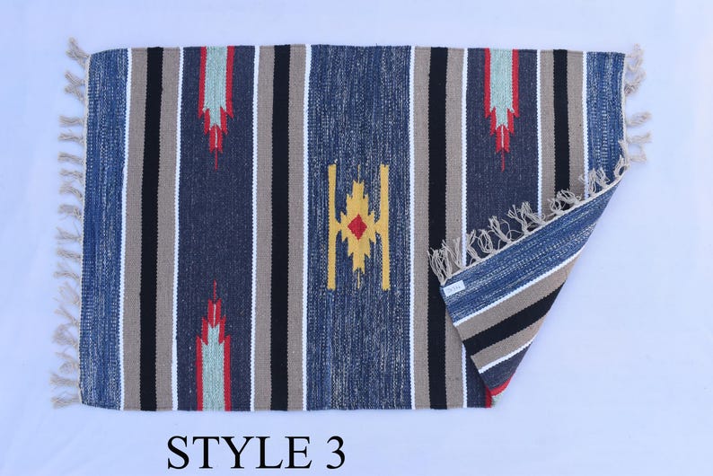 Puede incluir: Una alfombra rayada azul, beige, negro y rojo con un patr&oacute;n geom&eacute;trico. La alfombra tiene flecos en todos los lados. "STYLE 3" est&aacute; escrito debajo de la alfombra.