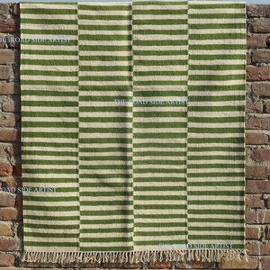 May include: A green and white striped rug with fringe on the edges. The rug is made of natural fibers and has a rustic look.