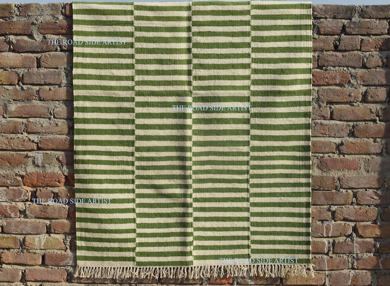 May include: A green and white striped rug with fringe on the edges. The rug is made of natural fibers and has a rustic look.