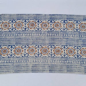May include: A blue and white cotton rug with a floral pattern and fringe. The rug has a brown and blue floral design.