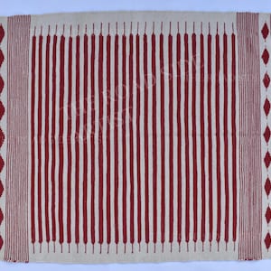 May include: Rectangular rug with a cream-colored background and vertical red stripes. The rug has a fringed edge and red diamond patterns on the sides. A decorative floor covering.