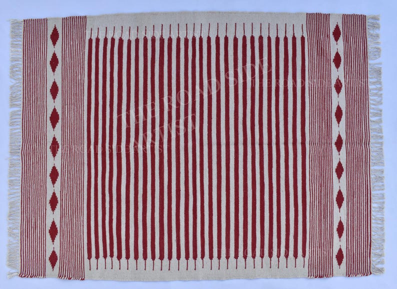 May include: Rectangular rug with a cream-colored background and vertical red stripes. The rug has a fringed edge and red diamond patterns on the sides. A decorative floor covering.