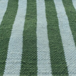 May include: A close-up of a green and white striped fabric. The fabric is woven with a textured pattern.