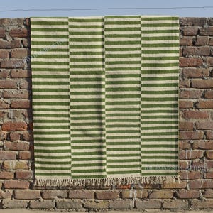 May include: A green and white striped rug with a fringe border. The rug is hanging on a brick wall.