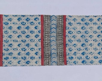 May include: A long, rectangular rug with a white background and a blue and black geometric pattern. The rug has red stripes on the sides and fringe on the ends.