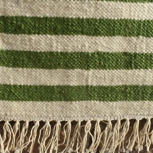 May include: A white and green striped rug with a fringe border. The rug is made of a woven material and has a natural, rustic look.