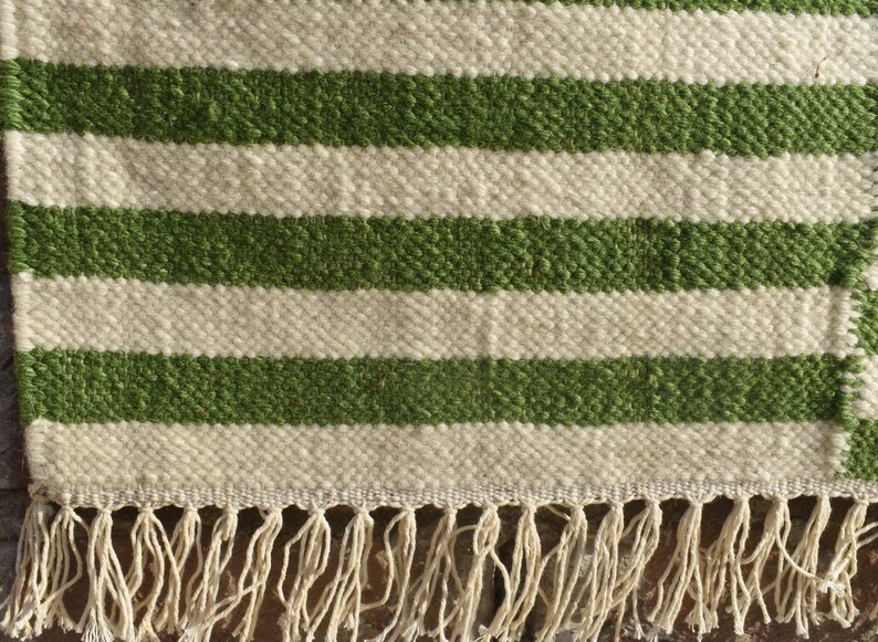 May include: A white and green striped rug with a fringe border. The rug is made of a woven material and has a natural, rustic look.