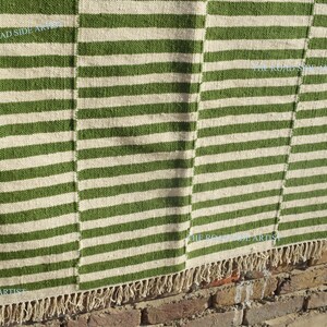 May include: A green and white striped rug with a fringe border. The rug is made of natural fibers and has a rustic look.