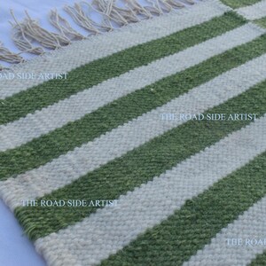 May include: A green and white striped rug with fringe on the edges. The rug is made of woven wool and has a rustic, handmade look.