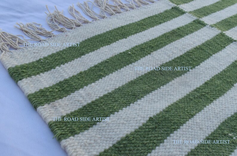 May include: A green and white striped rug with fringe on the edges. The rug is made of woven wool and has a rustic, handmade look.
