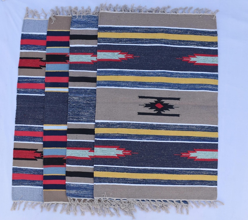 Puede incluir: Cuatro alfombras tejidas con un patr&oacute;n a rayas en tonos de azul, rojo, amarillo y beige. Las alfombras tienen flecos en los bordes.