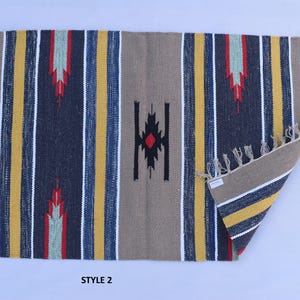 Puede incluir: Una alfombra tejida con un patr&oacute;n geom&eacute;trico en tonos de azul, amarillo, rojo y blanco. La alfombra tiene un borde de flecos y el texto "STYLE 2" est&aacute; impreso debajo de la alfombra.