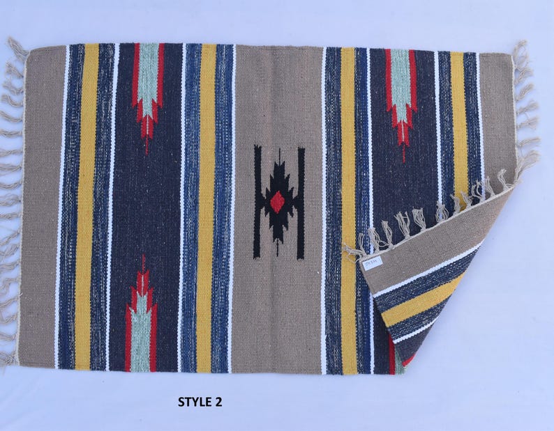 Puede incluir: Una alfombra tejida con un patr&oacute;n geom&eacute;trico en tonos de azul, amarillo, rojo y blanco. La alfombra tiene un borde de flecos y el texto "STYLE 2" est&aacute; impreso debajo de la alfombra.