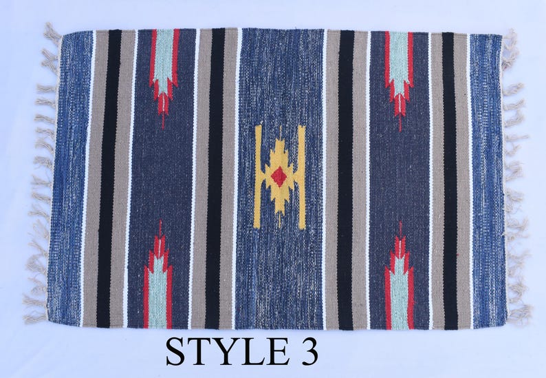 Puede incluir: Una alfombra rayada azul, gris y beige con un patr&oacute;n geom&eacute;trico en el centro. La alfombra tiene flecos en todos los lados. El texto "STYLE 3" est&aacute; impreso debajo de la alfombra.