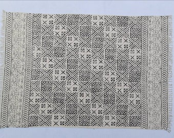 May include: A white cotton rug with a black geometric pattern. The pattern features squares, diamonds, and stars. The rug has fringe on all four sides.