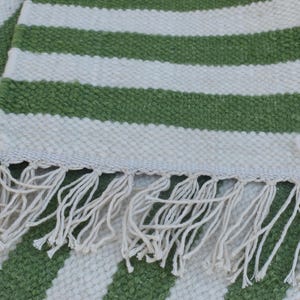 May include: A green and white striped rug with a fringe border. The rug is made of a woven material and has a soft, textured feel.