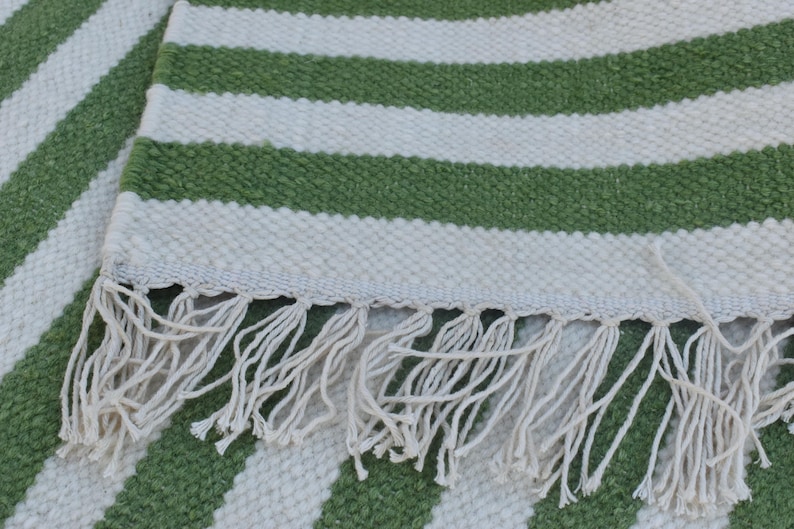 May include: A green and white striped rug with a fringe border. The rug is made of a woven material and has a soft, textured feel.