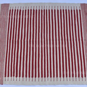 May include: A rectangular rug with a cream-colored background and vertical red stripes. The rug has a fringed edge and a decorative border with red diamond shapes. The text "THE ROADSIDE ARTIST" is visible.