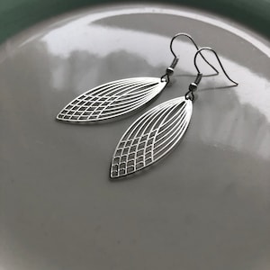 Può includere: Un paio di orecchini d'argento con un design geometrico. Gli orecchini hanno la forma di una foglia e un motivo delicato e intricato.