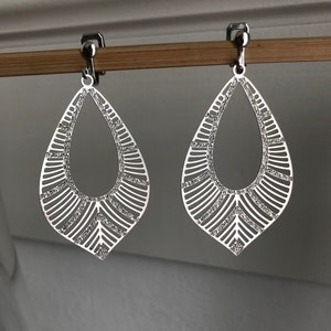 Könnte beinhalten: Ein Paar silberne Ohrclips mit geometrischem Design. Die Ohrringe sind tropfenförmig und haben ein zartes, filigranes Muster.