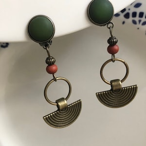 Könnte beinhalten: Ein Paar grüne und bronzene Ohrringe mit einem Kreis- und Halbkreisdesign. Die Ohrringe haben einen grünen Stein und eine braune Perle.