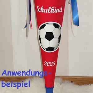 Op de afbeelding: Een rood en blauwe stoffen kegelvormige cadeautas met voetbalafbeeldingen, de naam Raphael, het woord Schulkind en het jaartal 2025. De bovenkant is samengebonden met witte en blauwe linten in een strik als decoratieve sluiting.
