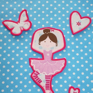 Könnte beinhalten: Applizierte Stoffformen einer Ballerina, eines Schmetterlings und Herzen mit rosa Einfassung. Die Ballerina trägt einen rosa Tütü und Ballettschuhe. Der Hintergrund ist ein hellblauer Stoff mit weißen Tupfen.