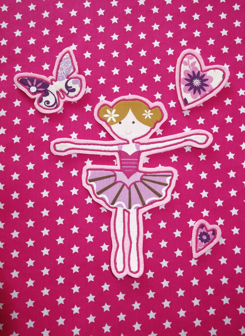 May include: Appliqu&eacute; set featuring a ballerina, butterfly, and hearts on a pink star-patterned background. The ballerina is in a ballet pose, wearing a pink tutu. The butterfly and hearts have floral patterns.